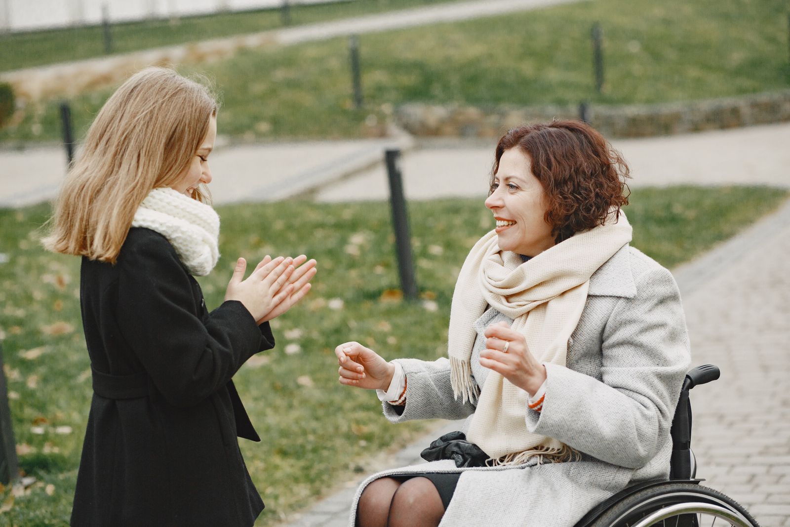 A woman in a wheelchair playing a clapping game with a young girl at the park
